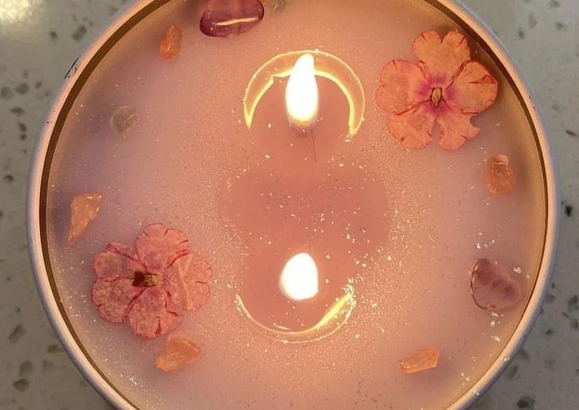 Vela encendida vista desde arriba, con flores rosas alrededor de dos llamas