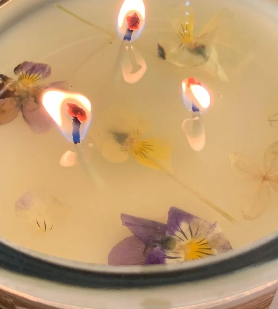 Vela encendida con dos pabilos entre flores prensadas