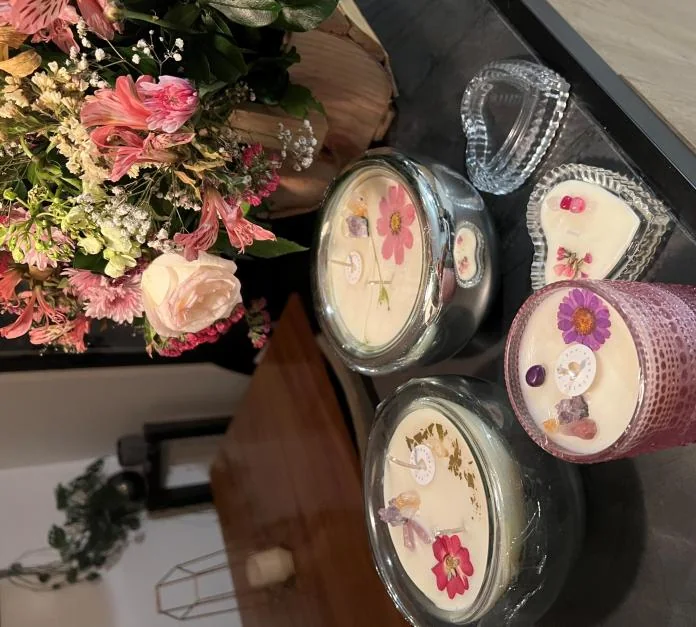Varias velas con flores prensadas sobre una mesa, con flores frescas detrás