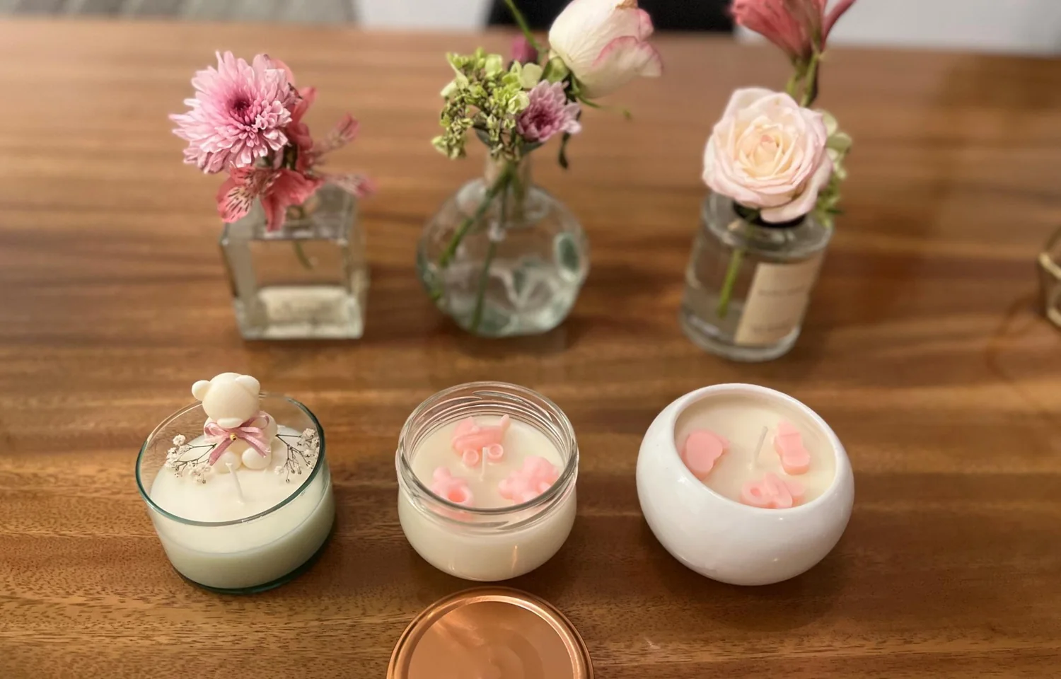 Tres velas Baby en recipiente de oso, tapa dorada y acabado perla, con flores detrás